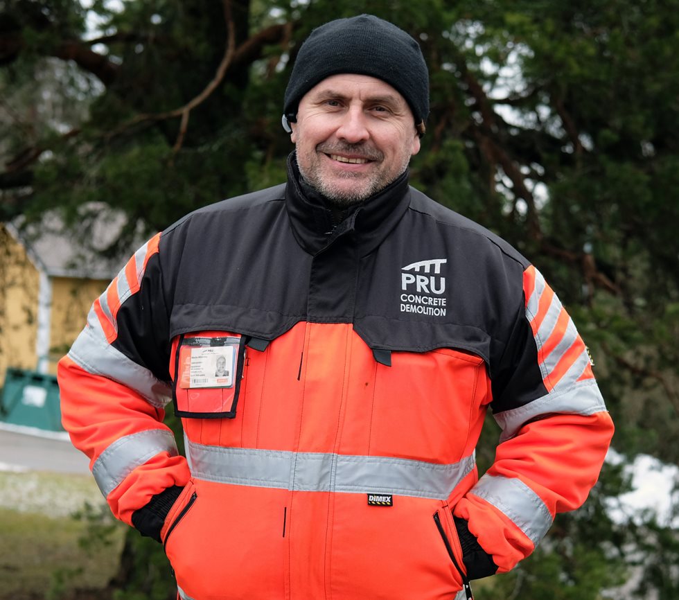 A man in orange working clothes standing in front of a tree.