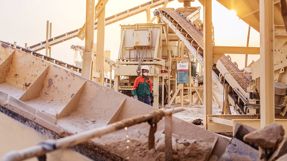 Man walking at the quarry next to crushing and conveying equiment.