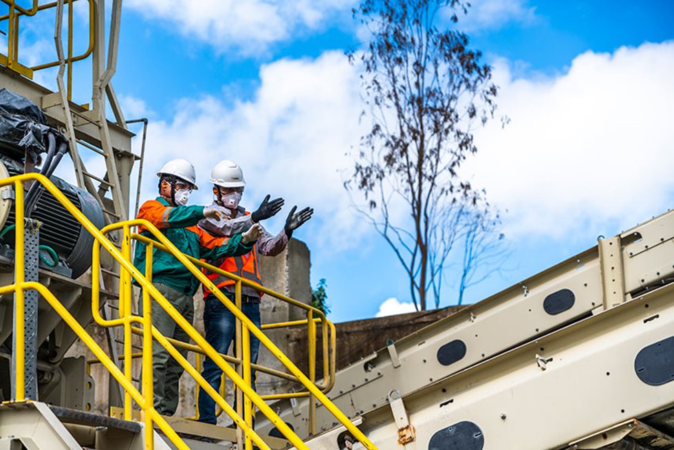 Two men discussing and pointing on top of crushing equipment. 